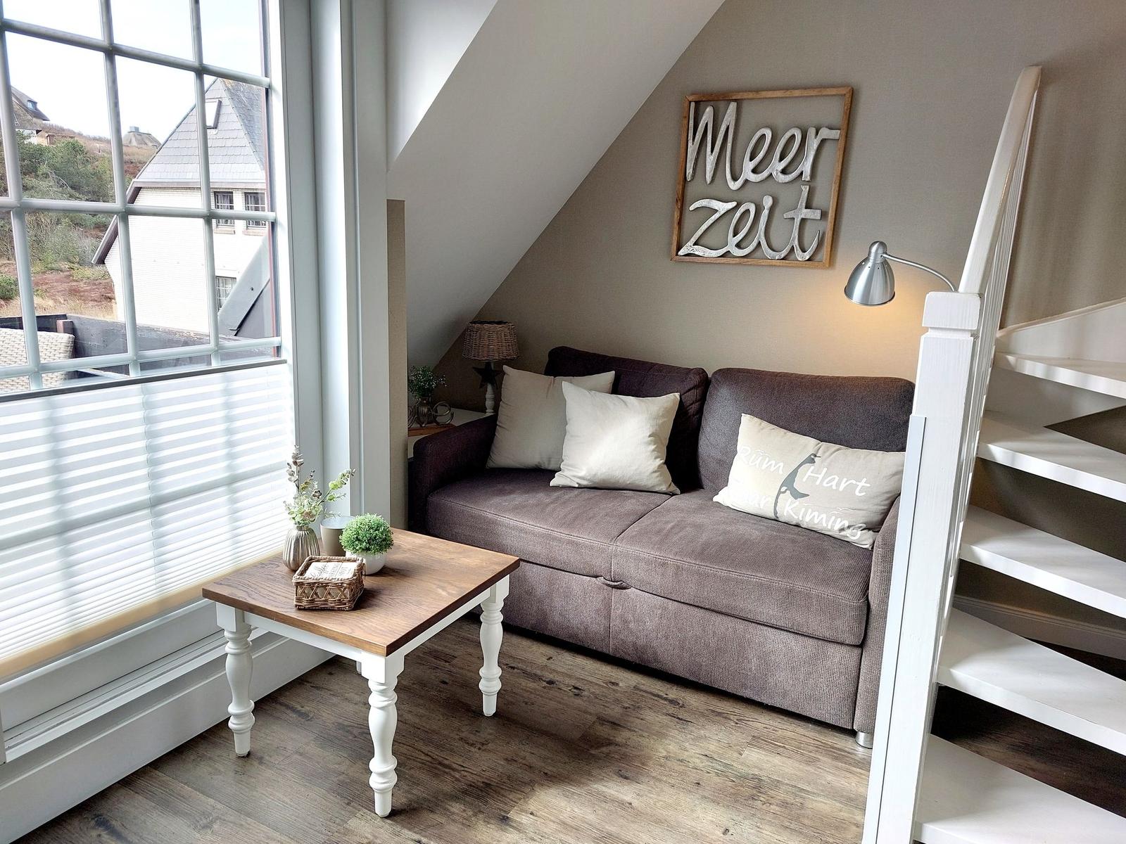 Ein Sofa mit Kissen, Tisch und Wanddekoration in einem Raum mit Dachschräge und Fenster.