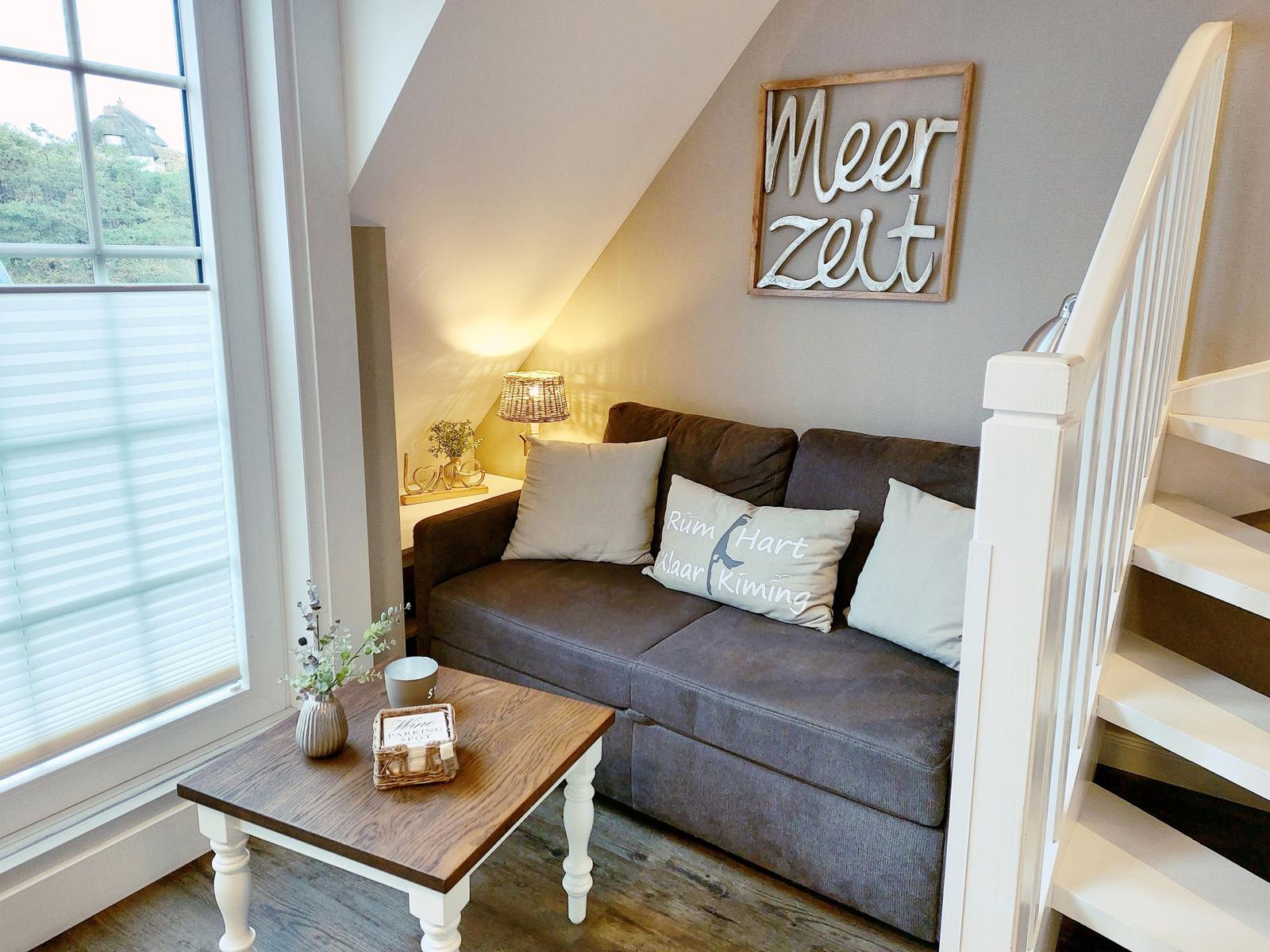 Ein Sofa mit Kissen unter einem Dachfenster neben einer Treppe.