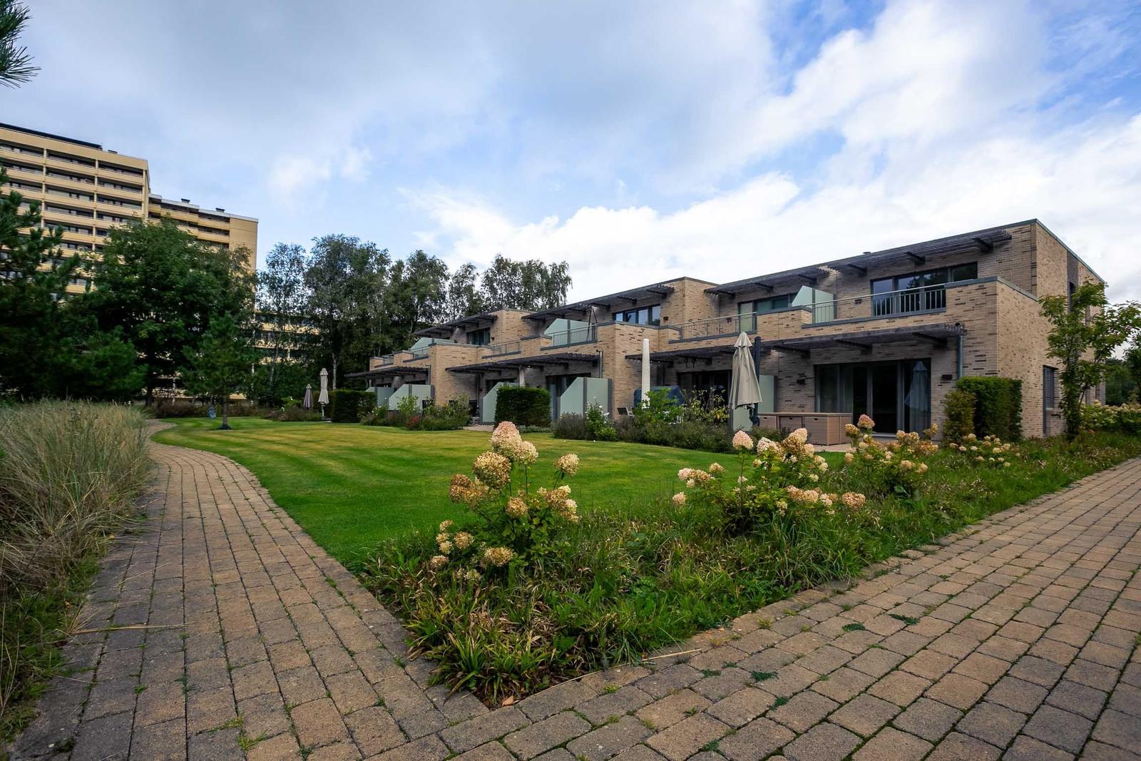Modernes Ferienhaus mit Balkon, Garten und gepflastertem Weg unter blauem Himmel.