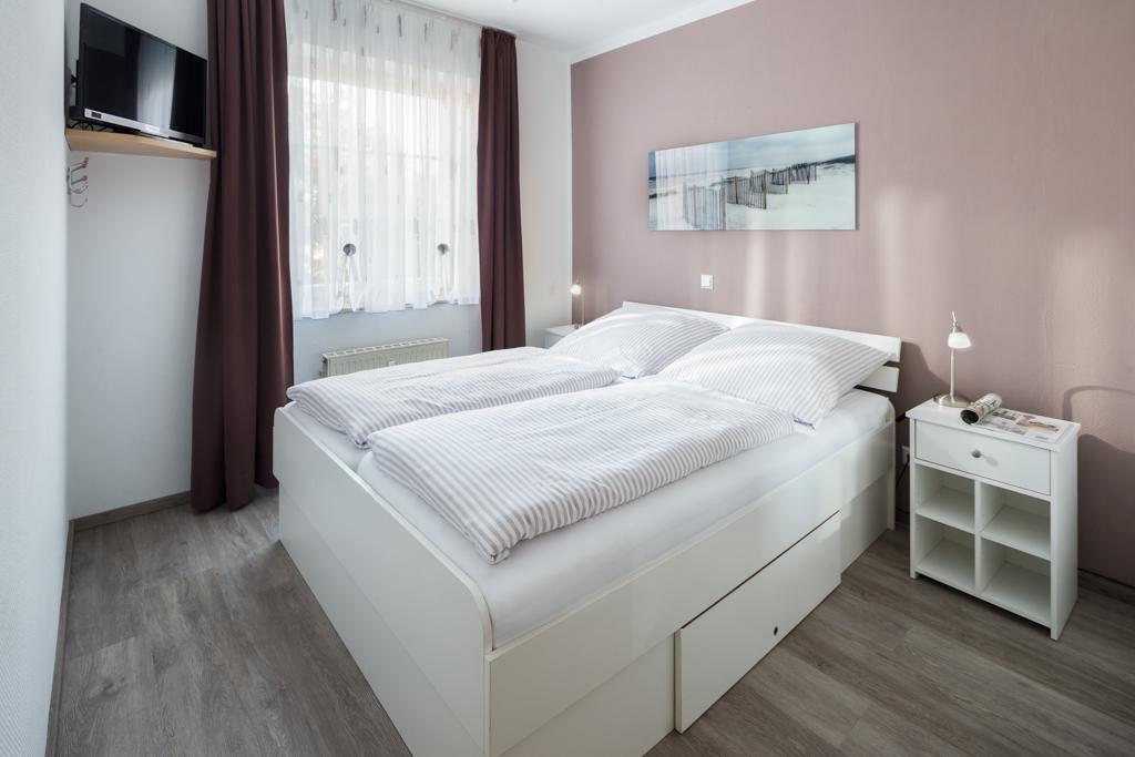 Schlafzimmer mit Doppelbett, Nachttisch und Fenster mit Vorhängen.