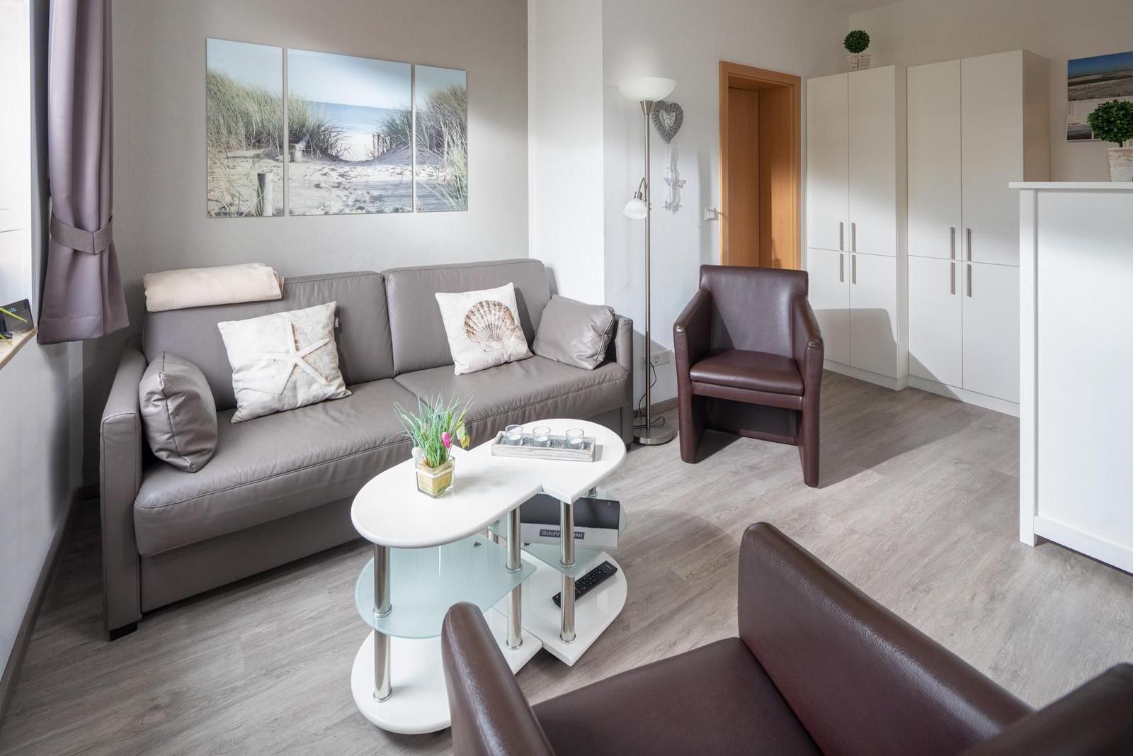 Wohnzimmer mit Sofa, zwei Sesseln und Tisch. Wandbild zeigt Strand.
