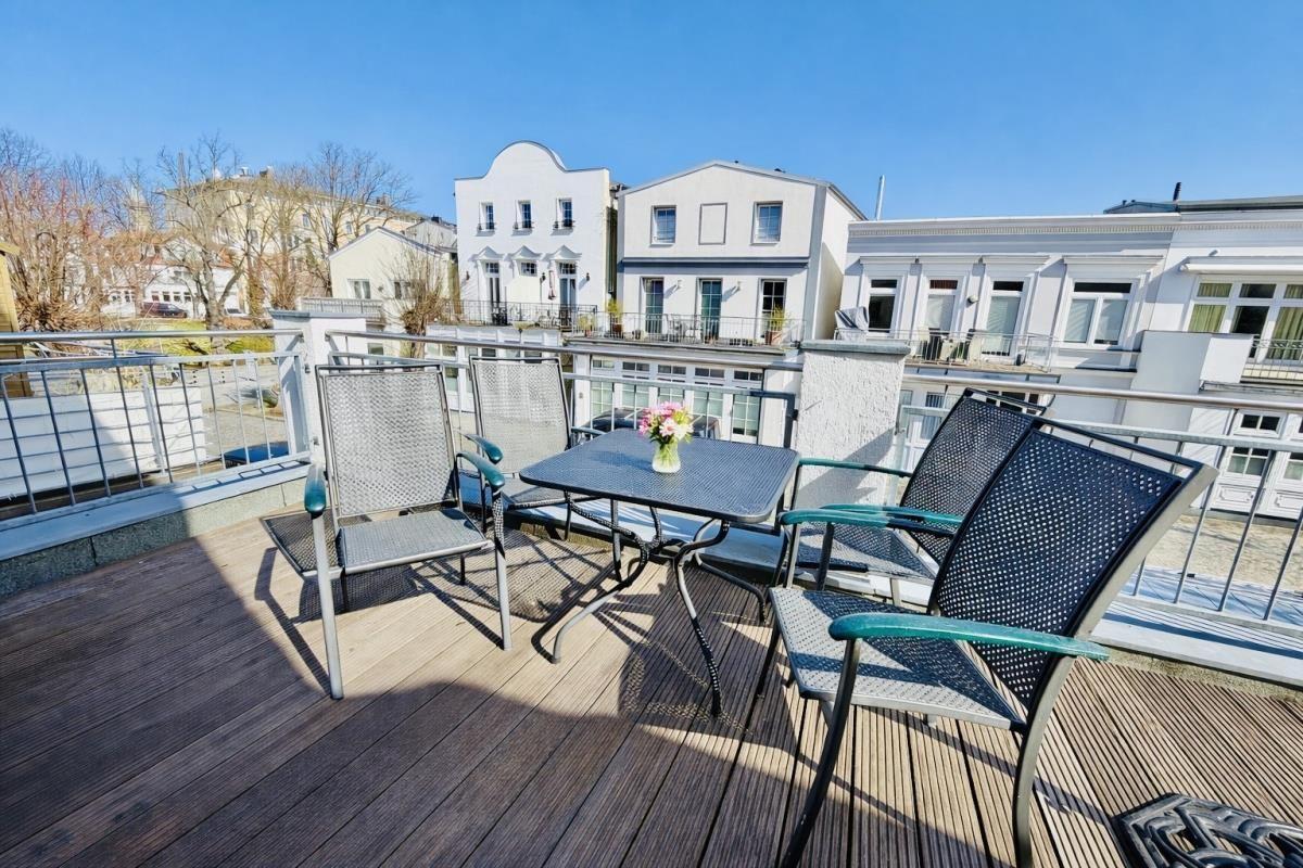 Terrasse mit Tisch und Stühlen, Blick auf weiße Gebäude.