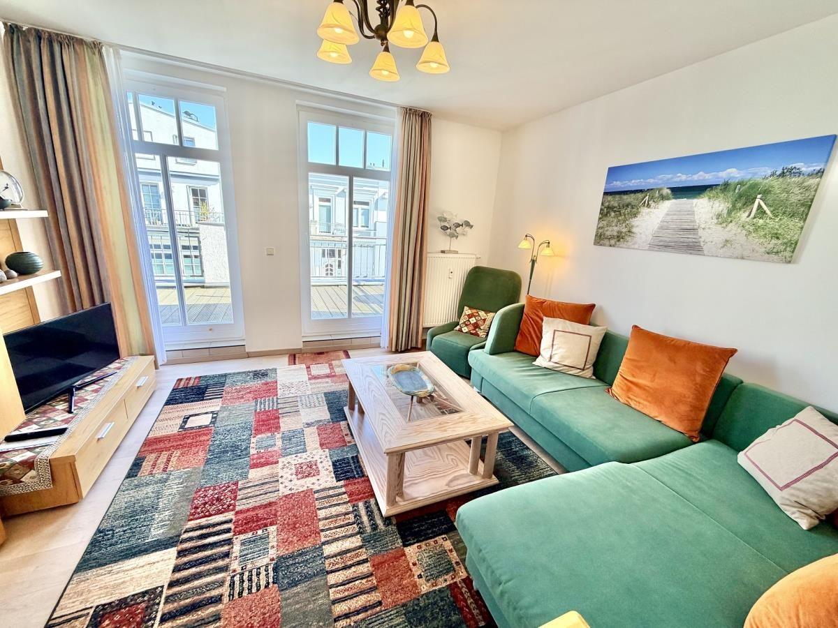 Wohnzimmer mit grünem Sofa, buntem Teppich und Fenstern zum Balkon.