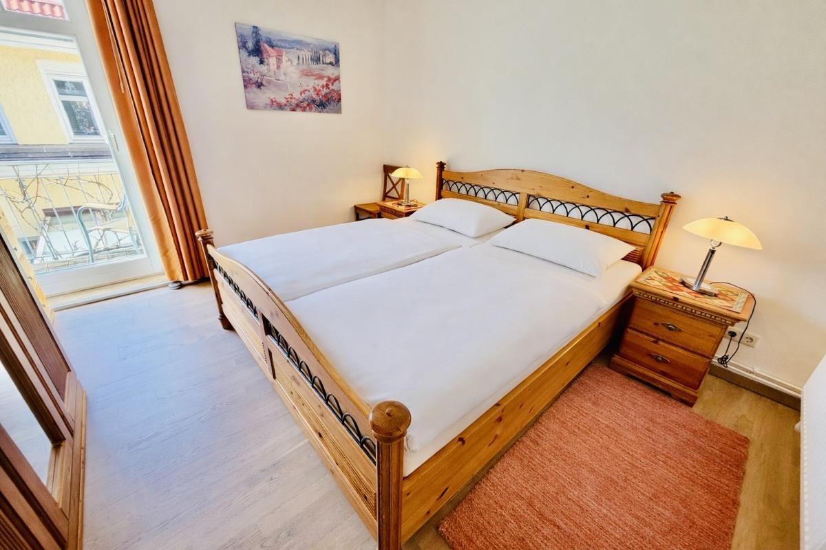 Doppelbett mit weißen Laken, zwei Nachttische mit Lampen, Bild an der Wand, Terrasse mit Blick.