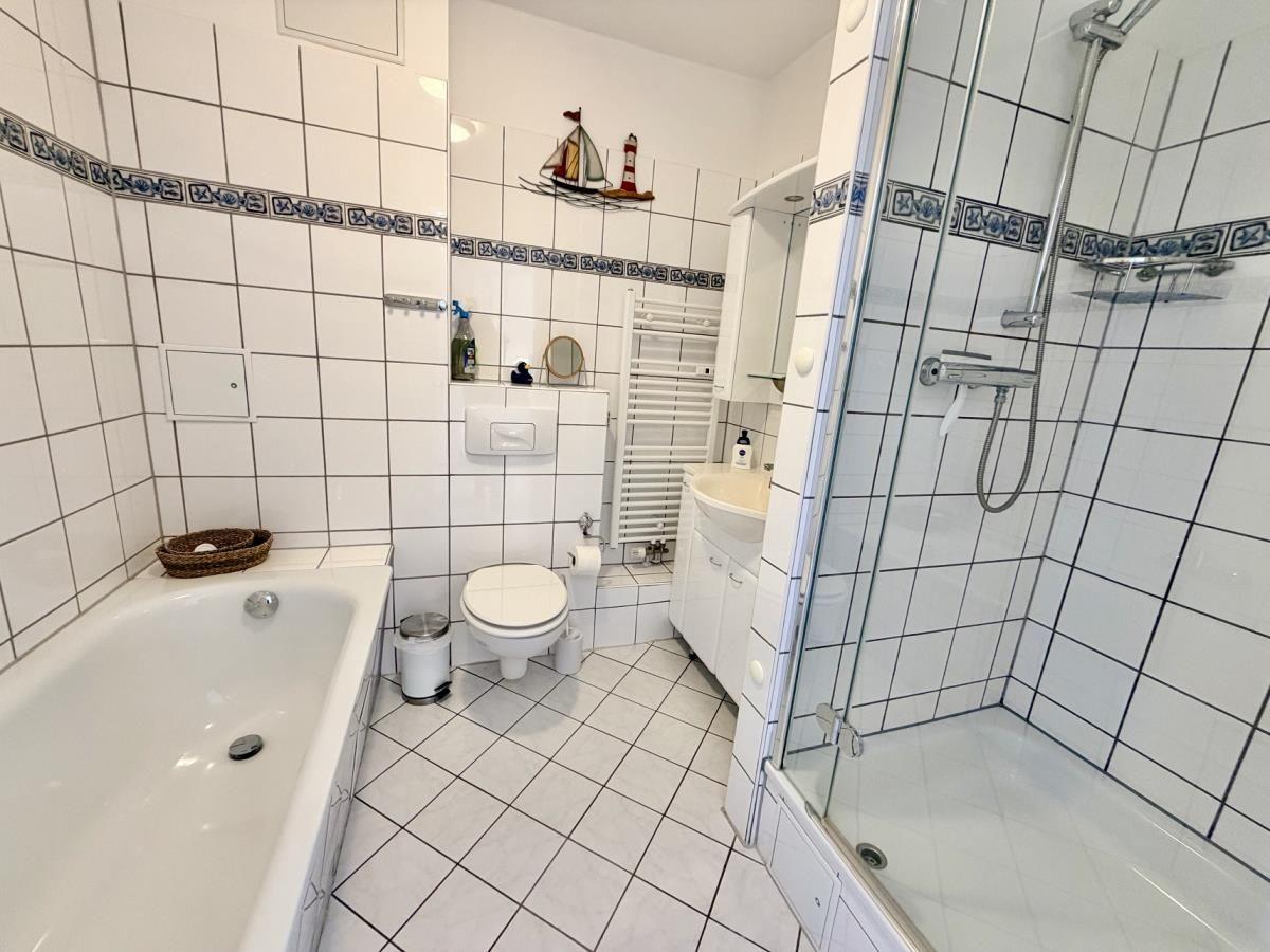 Badezimmer mit Badewanne, Dusche und Toilette. Weiße Fliesen und dekorative Bordüre.