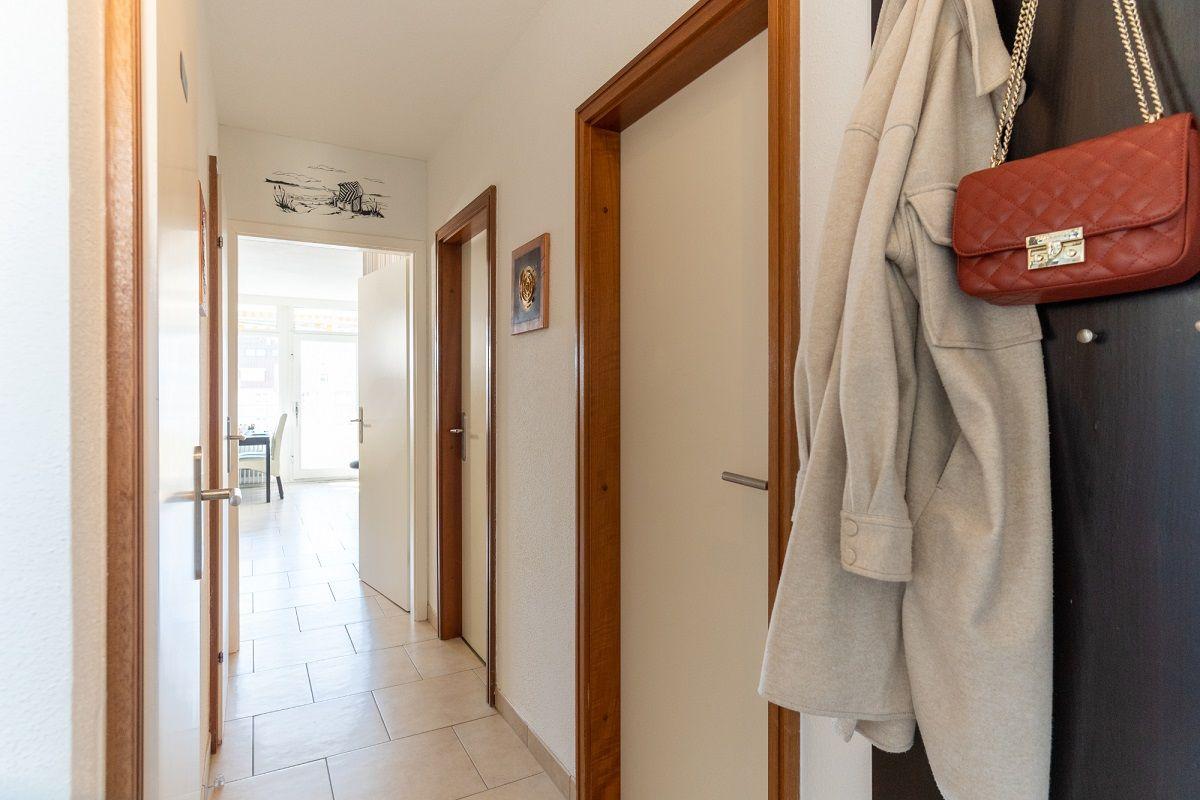 Flur mit Tür zu Wohnzimmer, Mantel und Handtasche hängen an Tür.