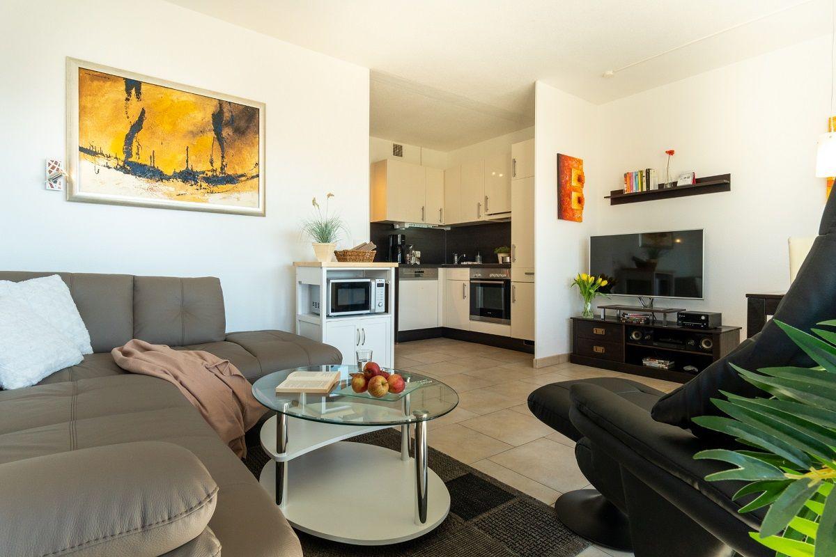 Wohnzimmer mit Sofa, Couchtisch und Küche im Hintergrund.