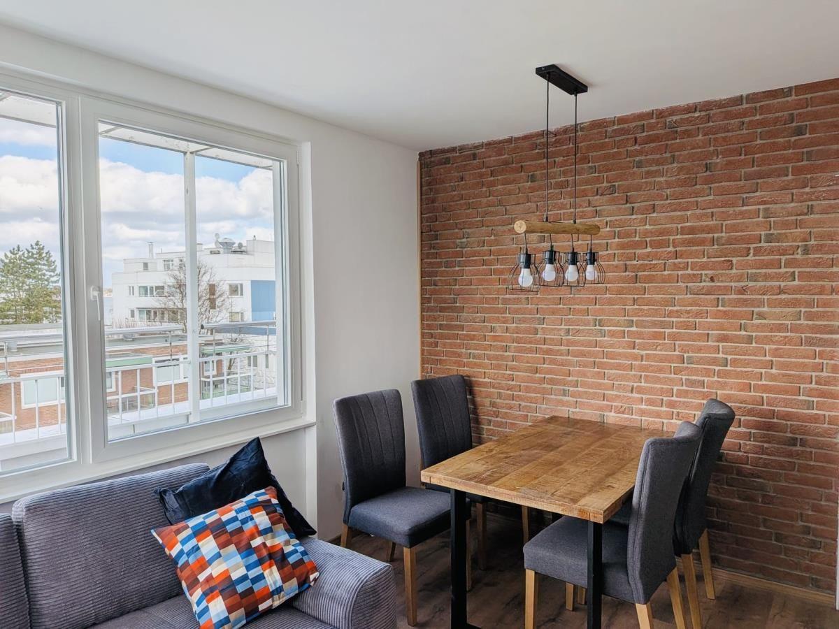 Essbereich mit Holztisch, vier Stühlen und Backsteinwand. Große Fenster mit Blick nach draußen.