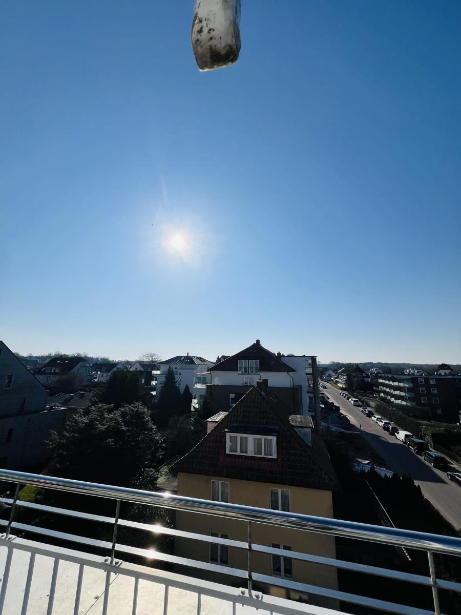Blick von Balkon auf städtische Umgebung unter blauem Himmel mit Sonne.