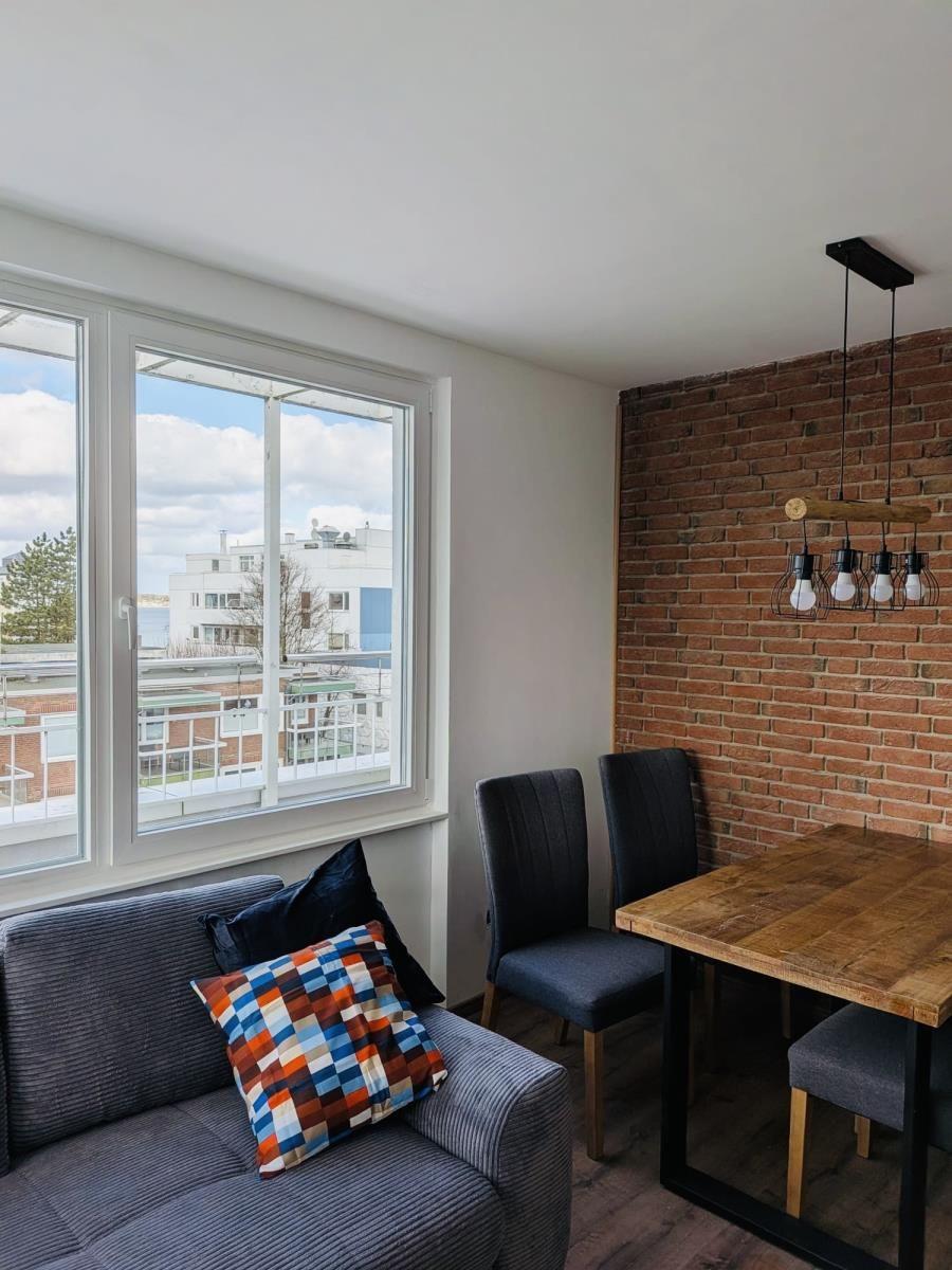 Raum mit Sofa, Tisch und Stühlen. Backsteinwand und Fenster mit Blick.