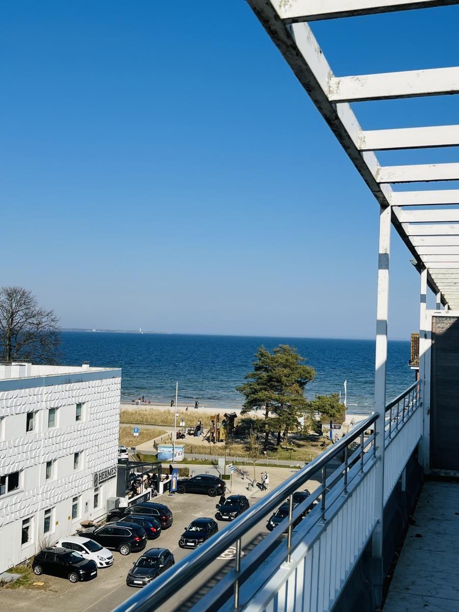 Blick von Balkon auf Strand und Meer mit Parkplatz und Gebäude.