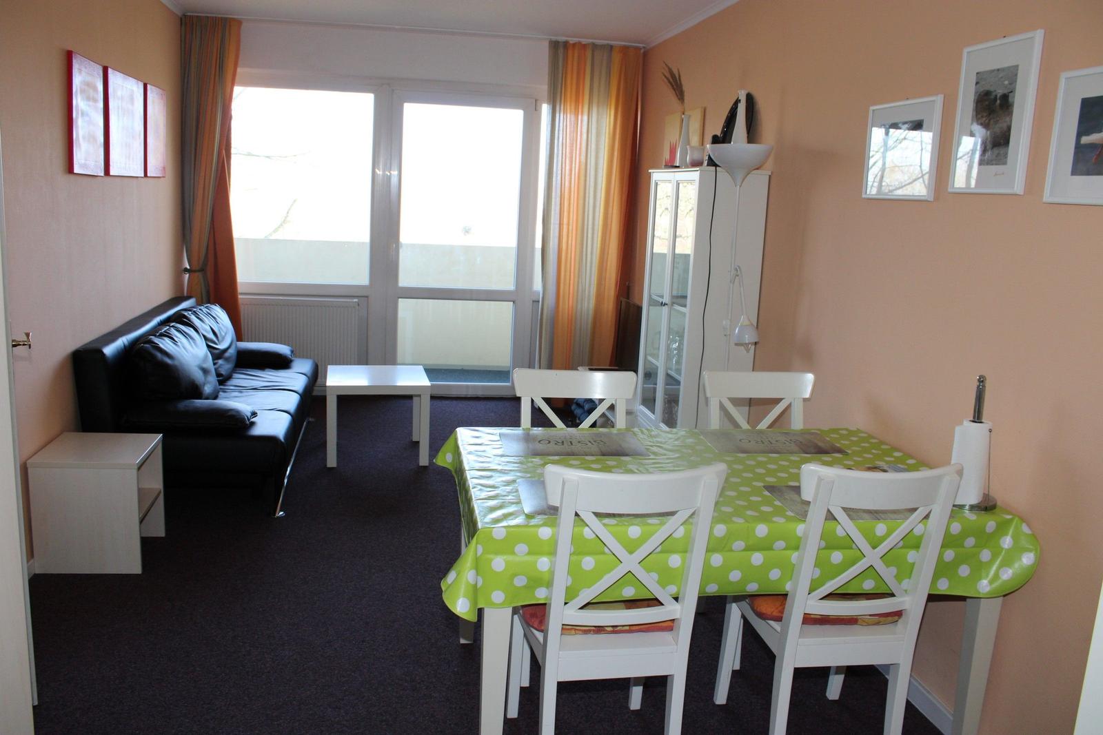 Wohn- und Essbereich mit Sofa, Tisch und Stühlen. Fenster mit Vorhängen.
