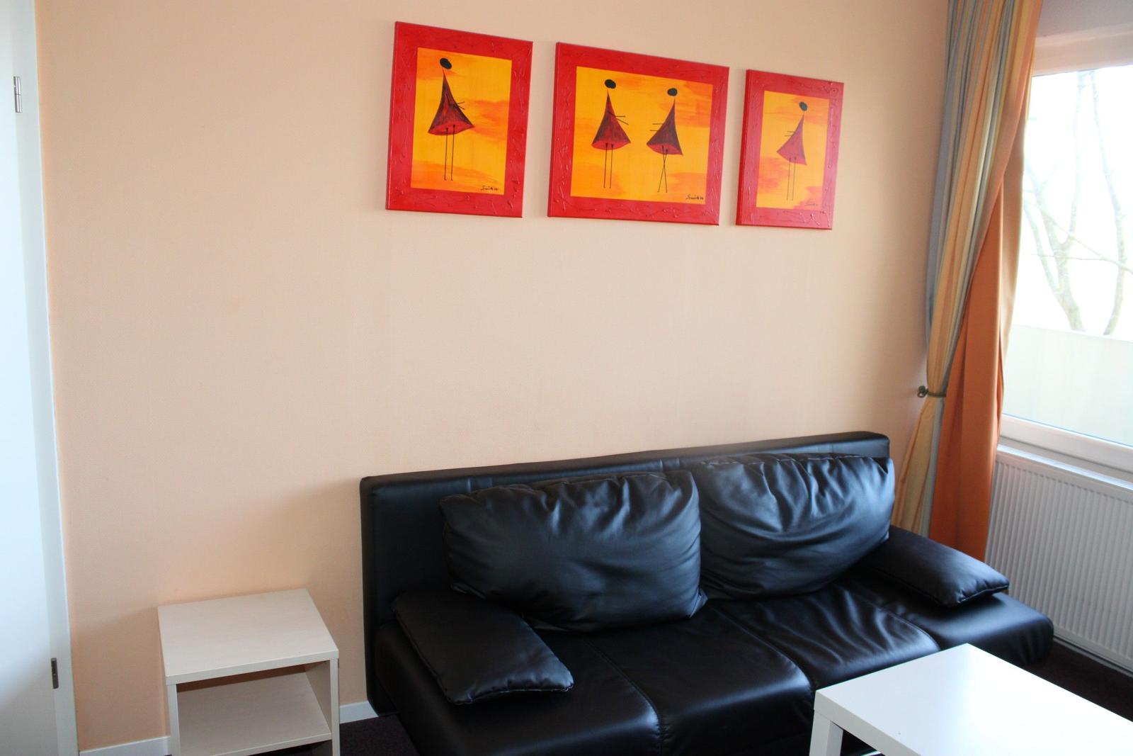 Schwarzes Sofa mit Kissen, Wandbilder und Fenster mit Vorhängen.
