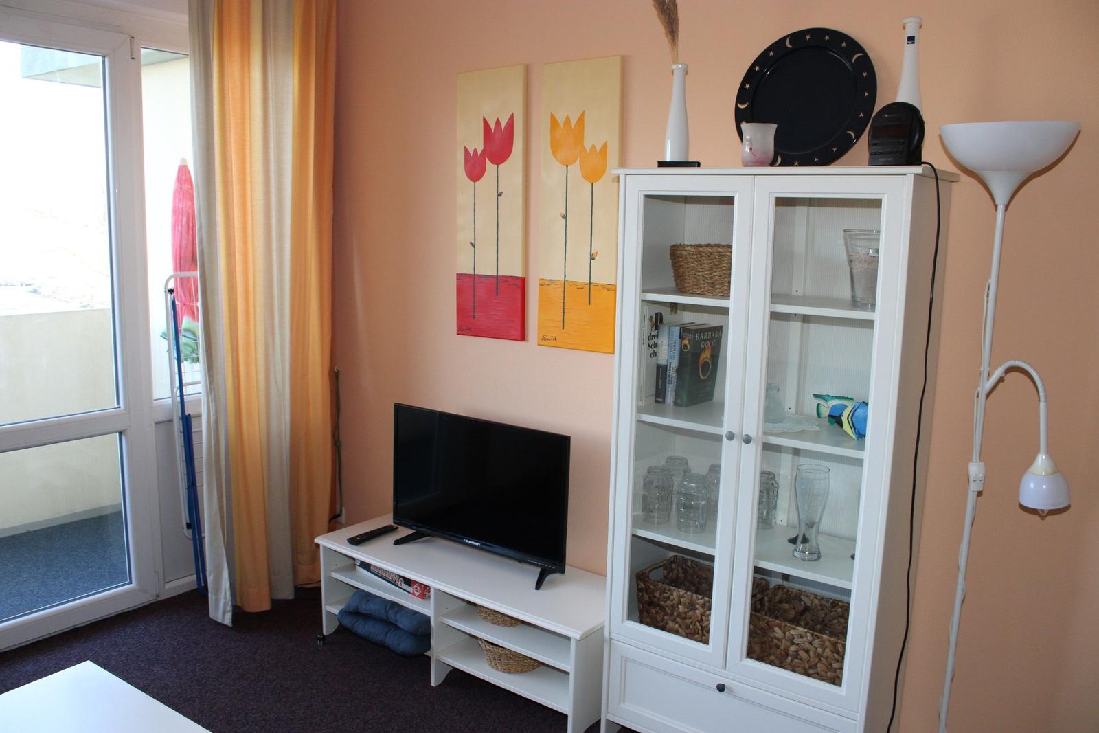 Wohnzimmer mit Fernseher, Glasvitrine und Fenster zur Terrasse.
