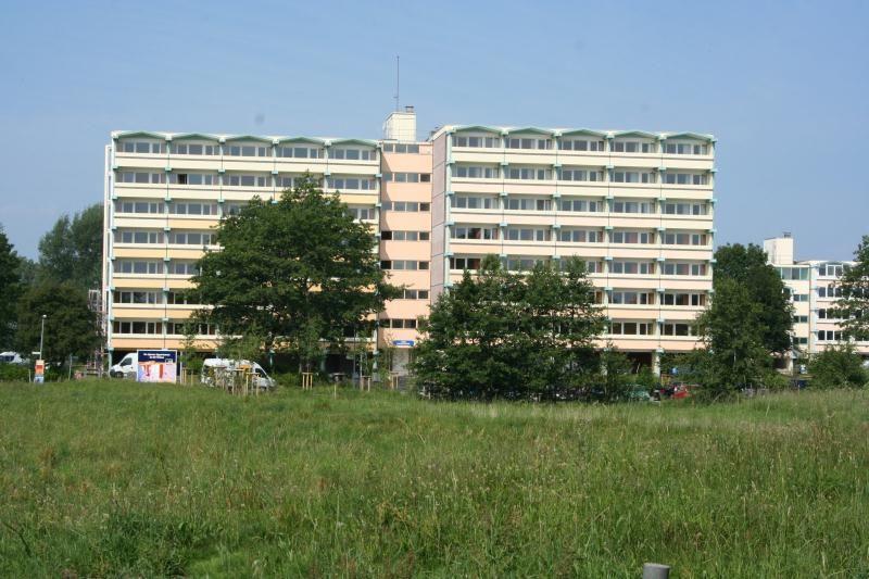 Hochhaus mit mehreren Stockwerken und Fenstern, umgeben von Bäumen und Gras.