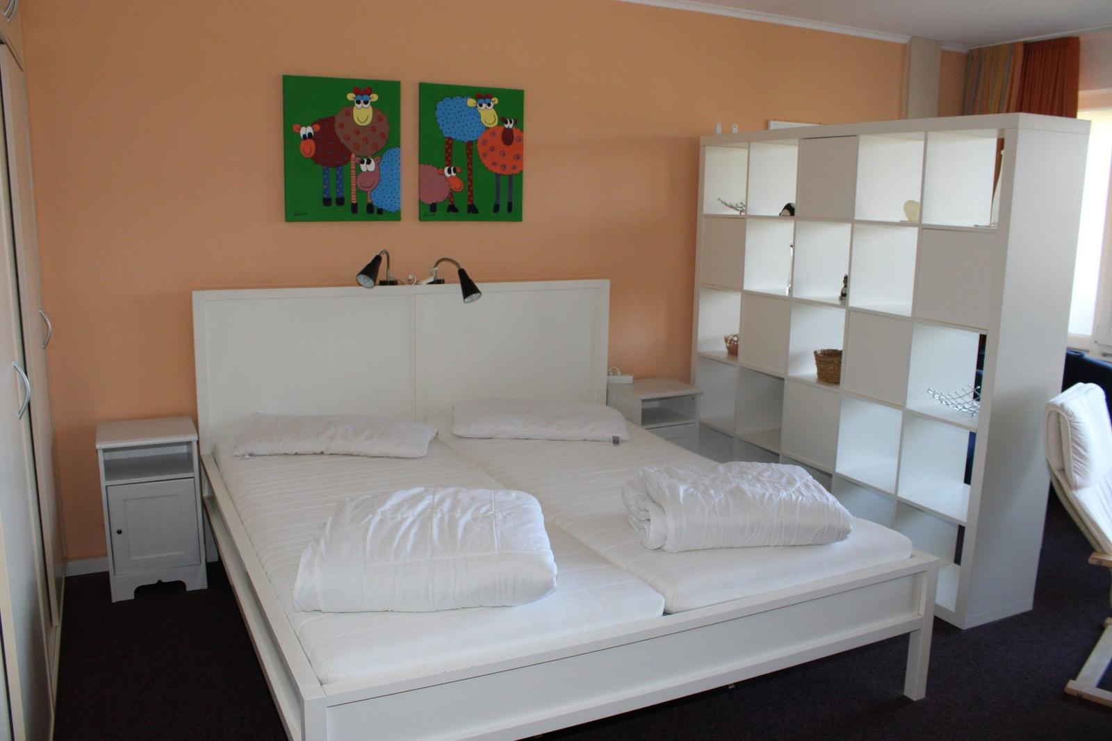 Schlafzimmer mit Doppelbett, weißen Möbeln und Wandbildern von Schafen.
