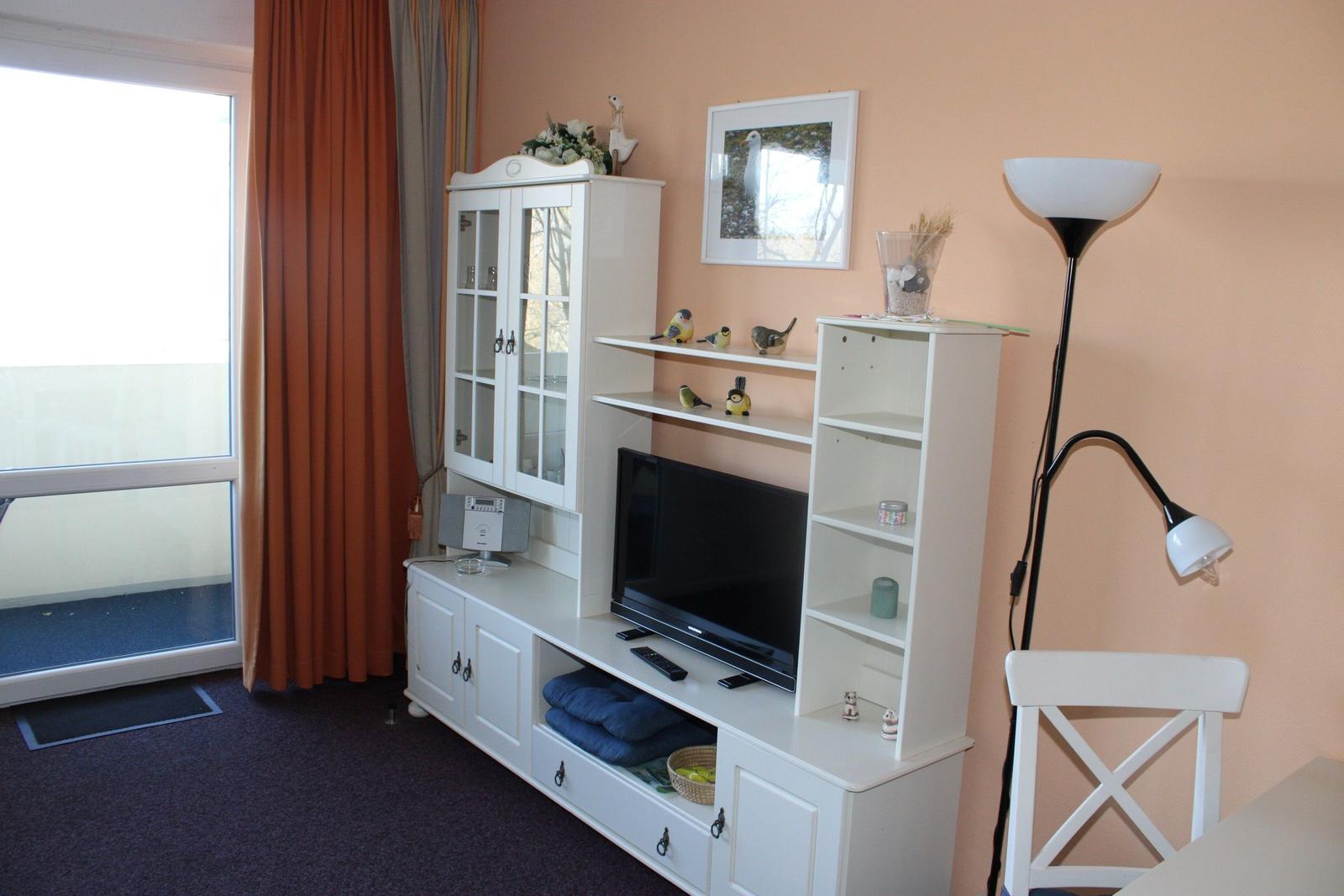 Wohnzimmer mit TV, weißen Schränken und Balkontür.