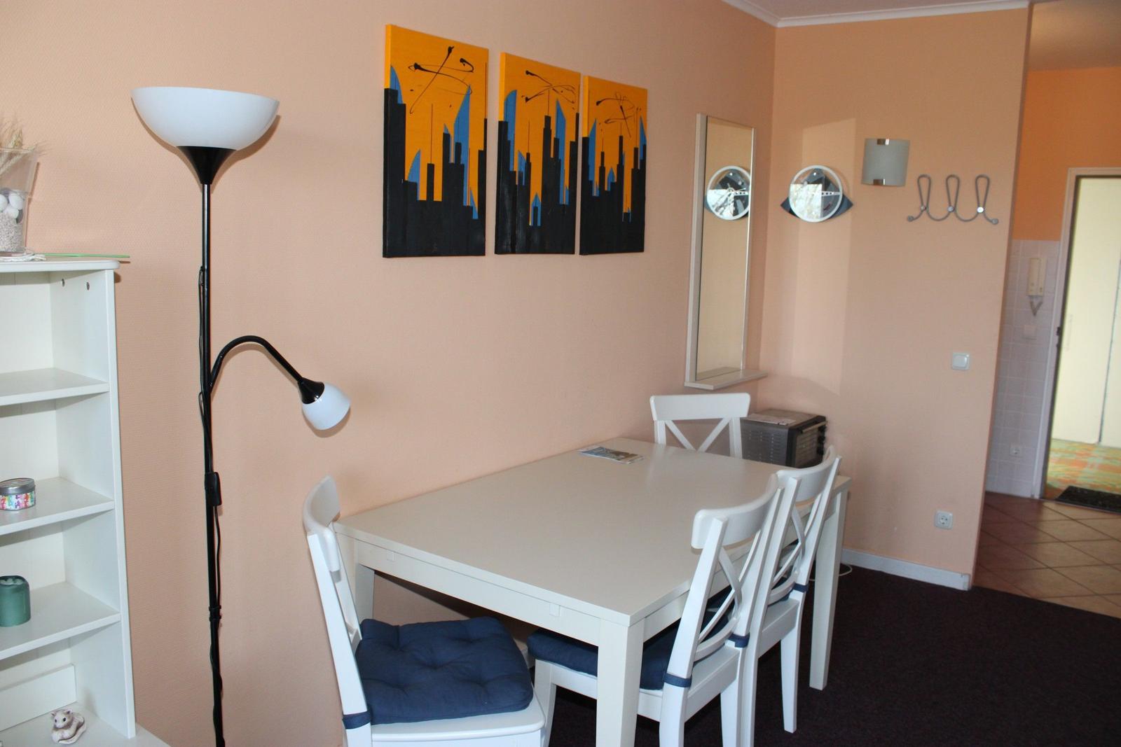 Essbereich mit weißem Tisch und Stühlen, Wandbildern und Stehlampe.