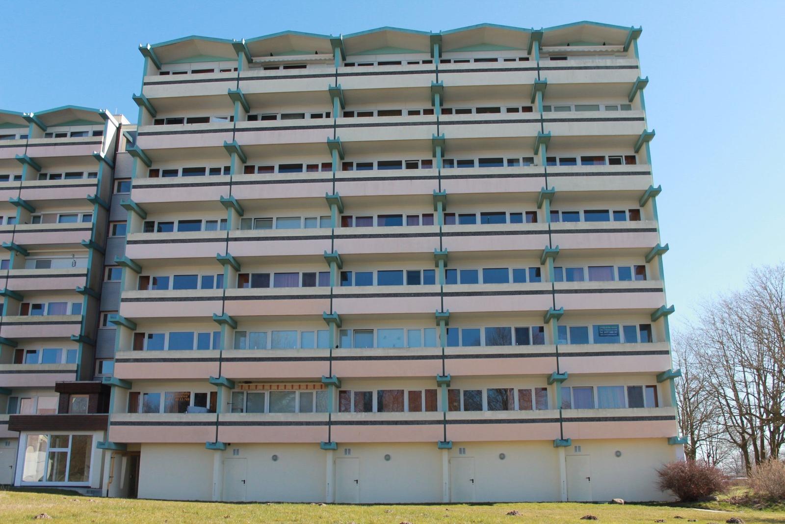 Hochhaus mit Balkonen und Fenstern, grüner Rasen im Vordergrund.