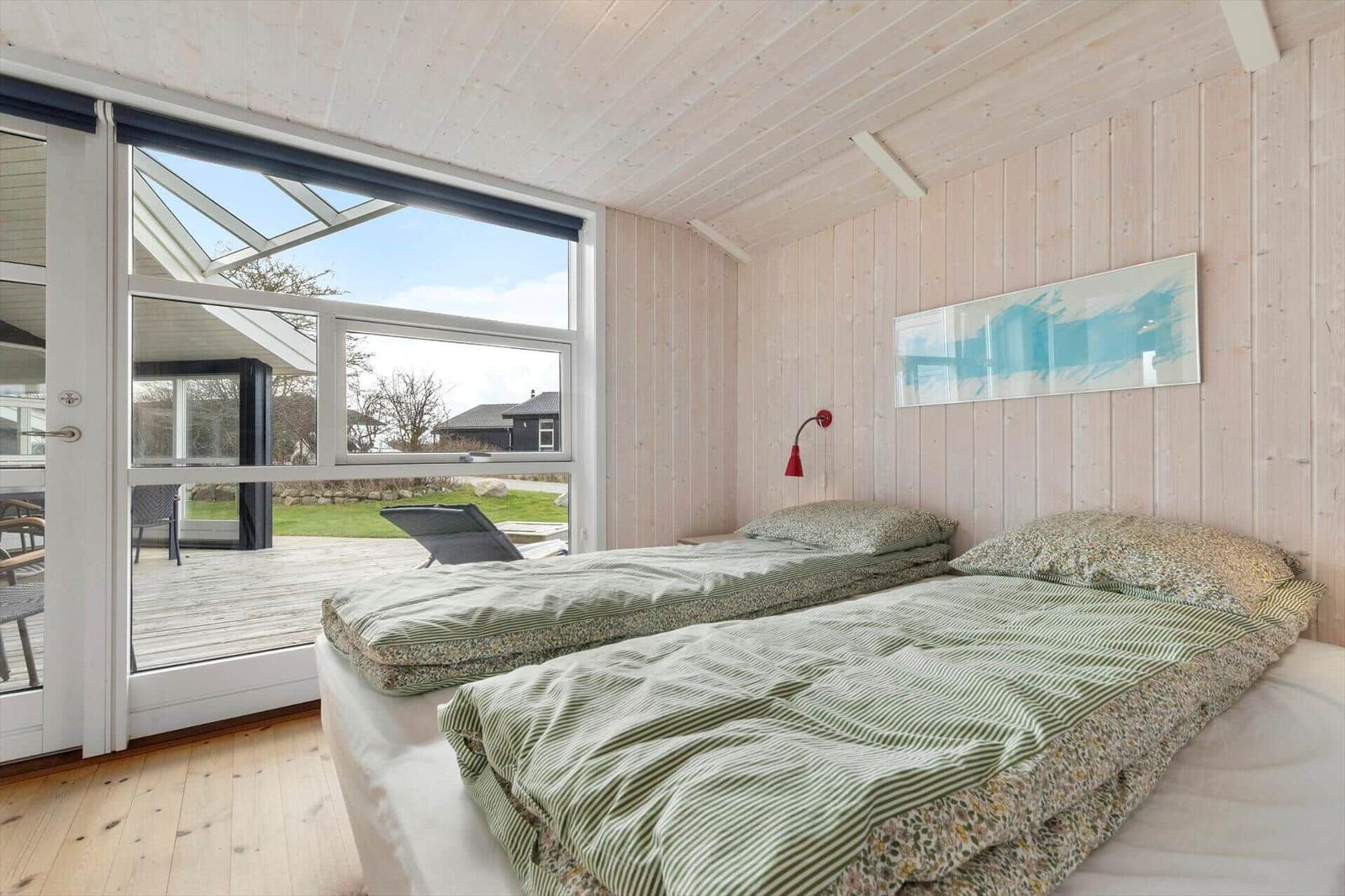 Zwei Betten mit grün gestreiften Bettwäsche. Holzwände und große Fenster mit Blick auf die Terrasse.