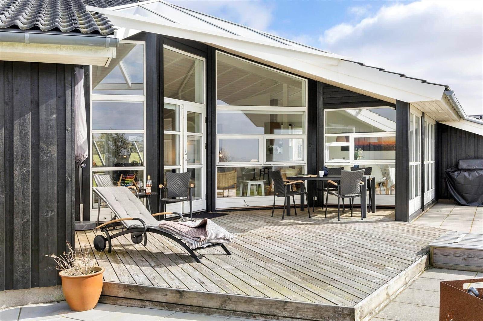 Terrasse mit Liegestuhl und Esstisch unter großem Glasbereich.