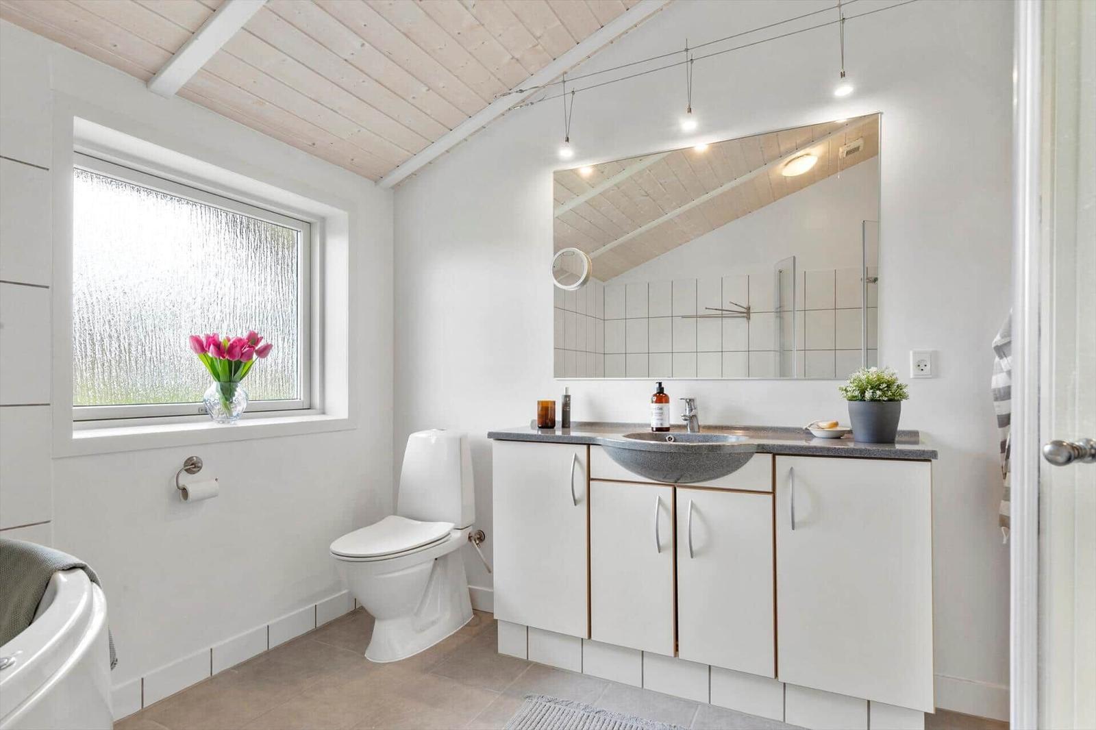 Badezimmer mit Waschbecken, Toilette und Fenster mit Blumen.