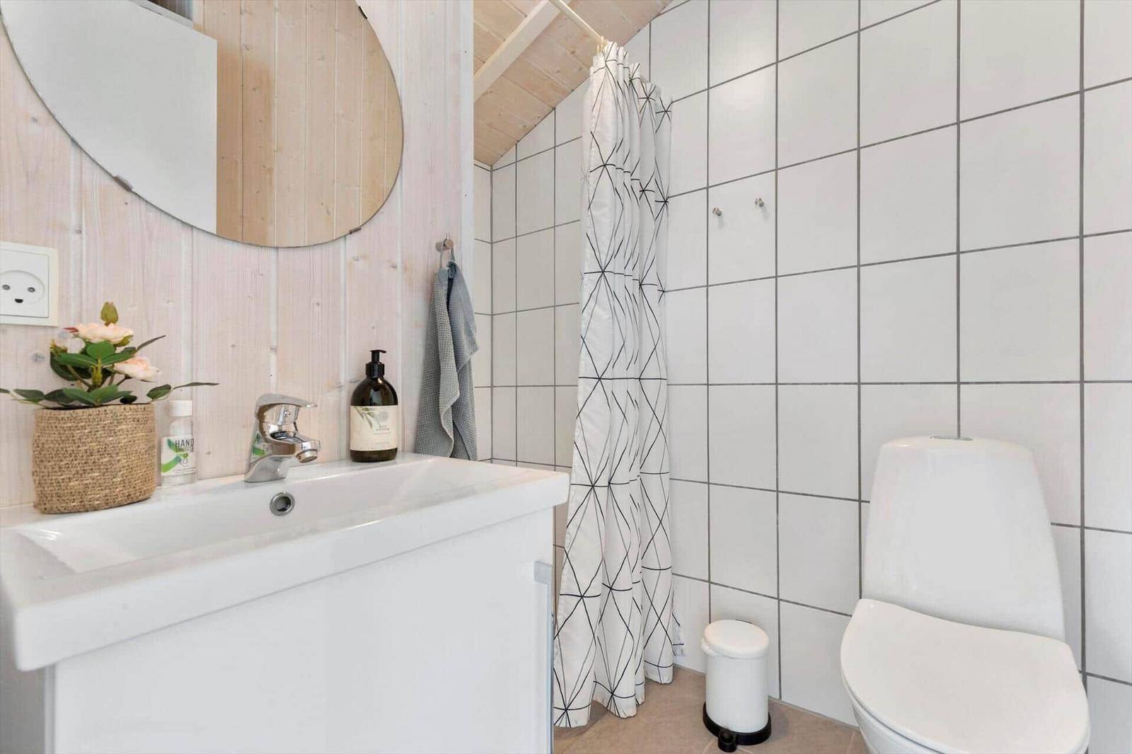 Badezimmer mit Waschbecken, Dusche und Toilette. Holzwand, Spiegel und Duschvorhang.