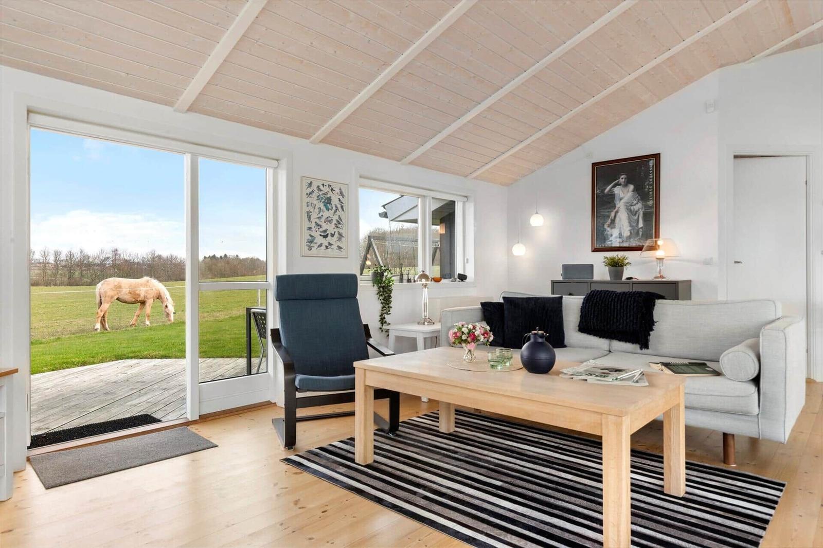 Wohnzimmer mit Sofa, Tisch und Blick auf Grasland mit Pferd.