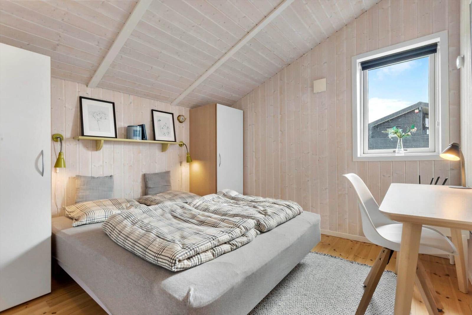 Schlafzimmer mit Bett, Schreibtisch und Fenster. Holzwände und Decke.