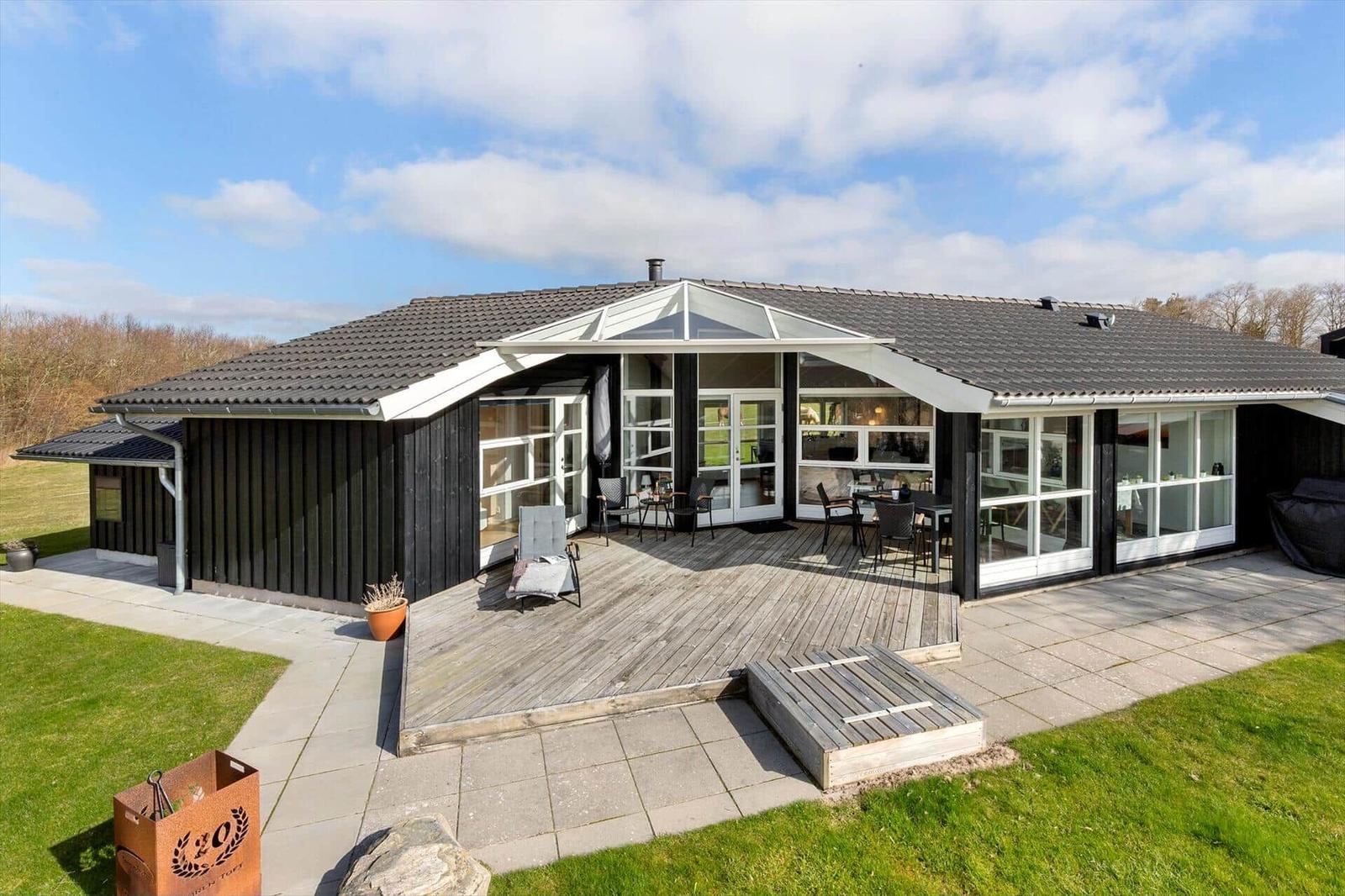 Moderne Villa mit großem Holzterrasse und Glasfronten. Grünflächen und Gartenbereich.