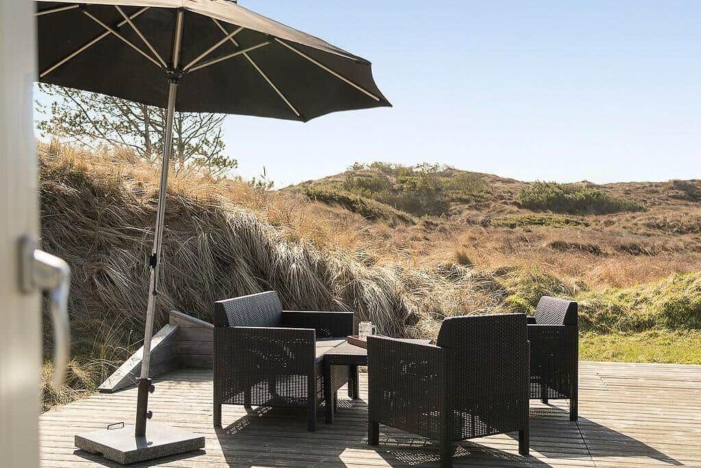 Terrasse mit Sitzgruppe und Sonnenschirm. Blick auf Dünenlandschaft.