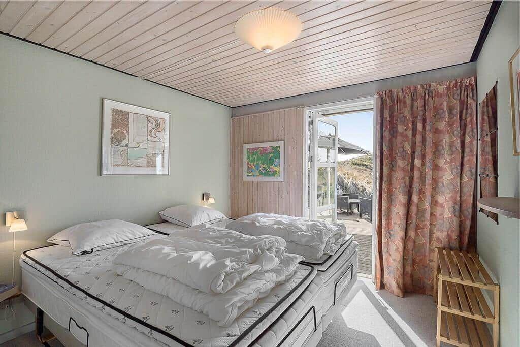 Schlafzimmer mit Doppelbett, Fenster und Vorhang.