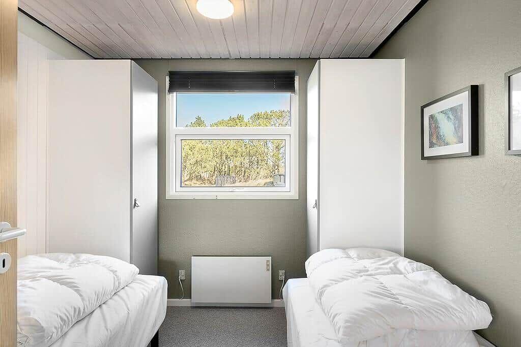 Zwei Betten, Fenster mit Blick auf Bäume, weiße Schränke und Heizung.