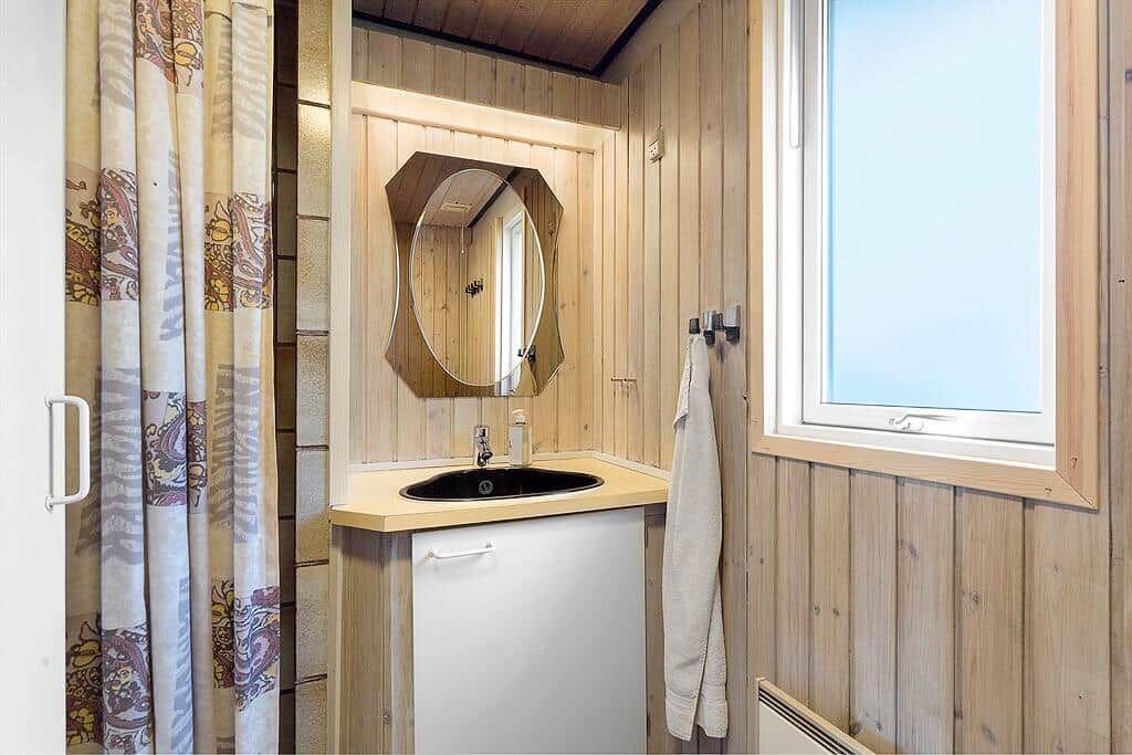 Badezimmer mit Holzwand, Waschbecken, Spiegel und Fenster