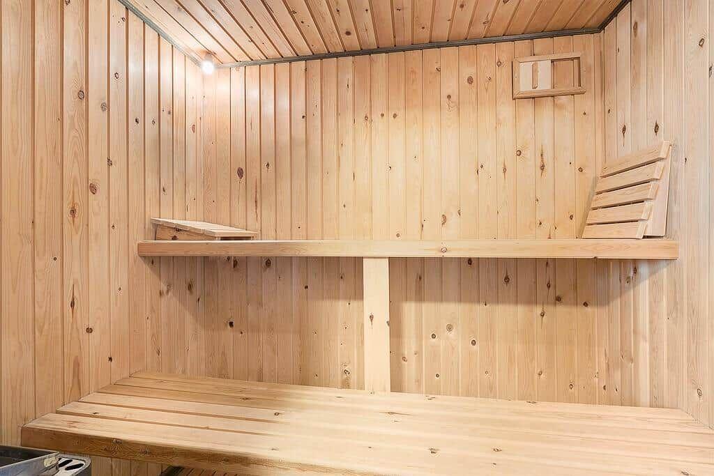 Holzsauna mit mehreren Sitzbänken und einer Wandöffnung.