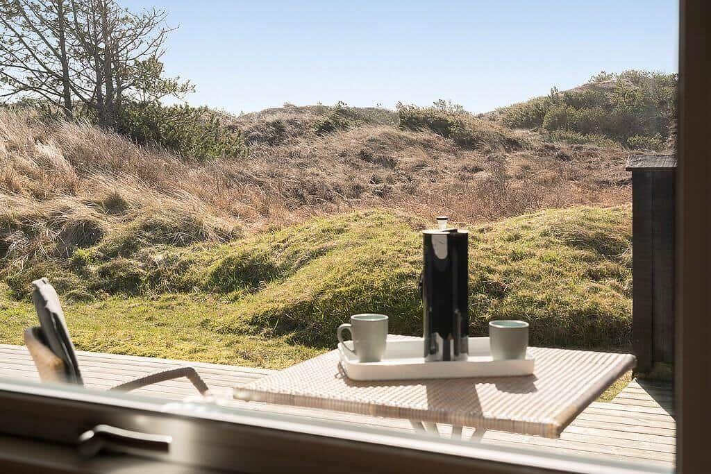 Auf der Terrasse steht ein Tablett mit Kaffeekanne und Tassen. Blick auf grasbewachsene Hügel.