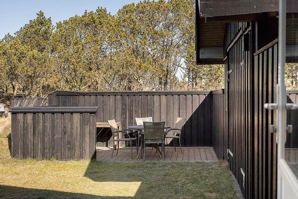 Hinterhof mit Tisch, Stühlen und Holzzaun. Grasfläche und Bäume im Hintergrund.