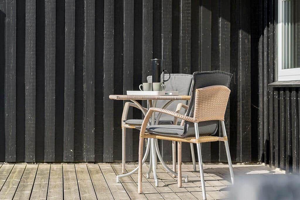 Terrasse mit Tisch und zwei Stühlen vor schwarzem Holzhaus