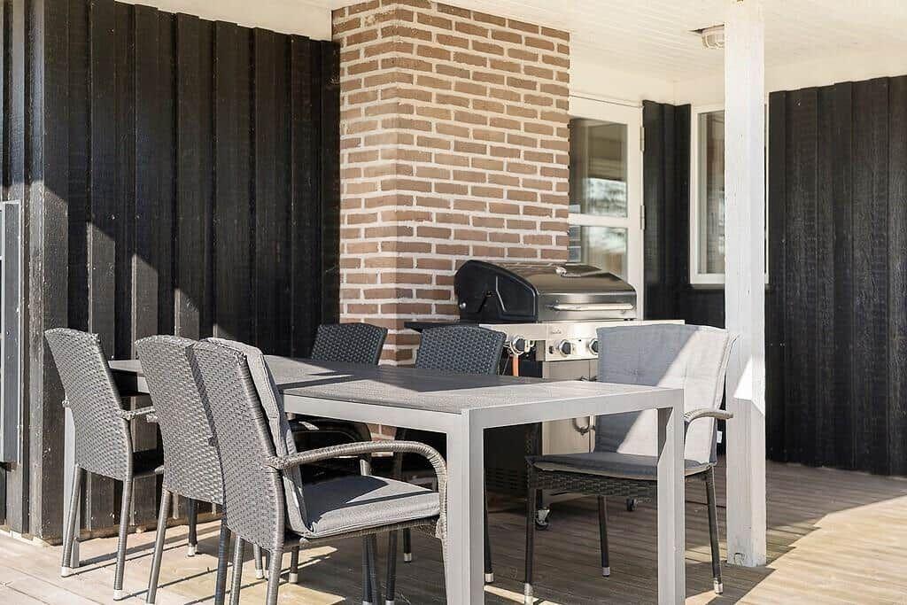 Terrasse mit Tisch, Stühlen und Grill an der Hauswand.