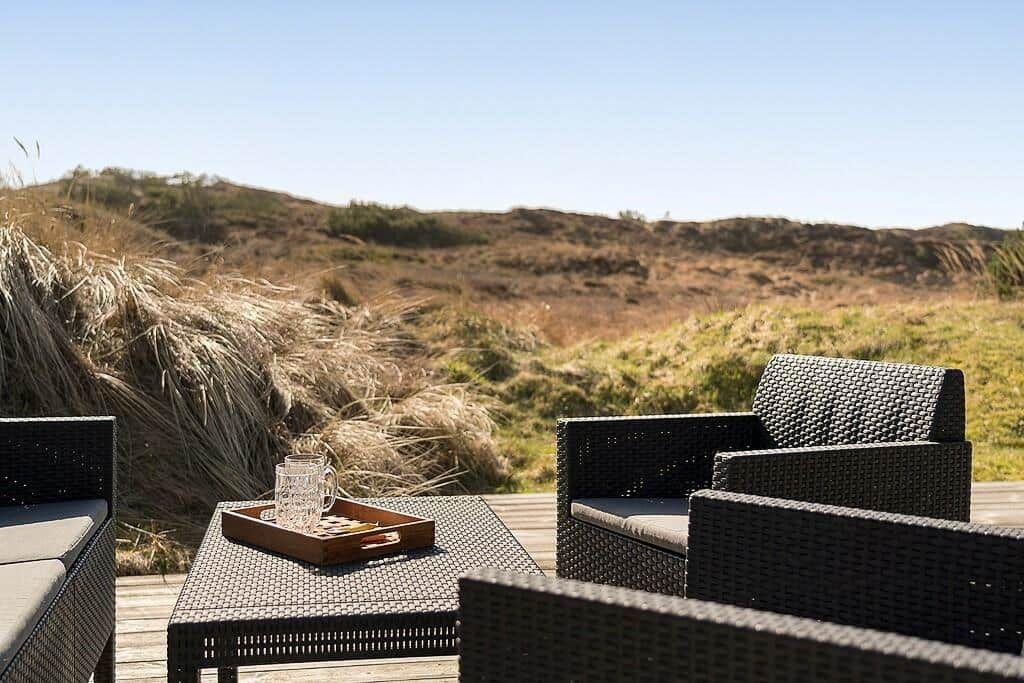 Terrasse mit Gartenmöbeln und Blick auf Dünenlandschaft.