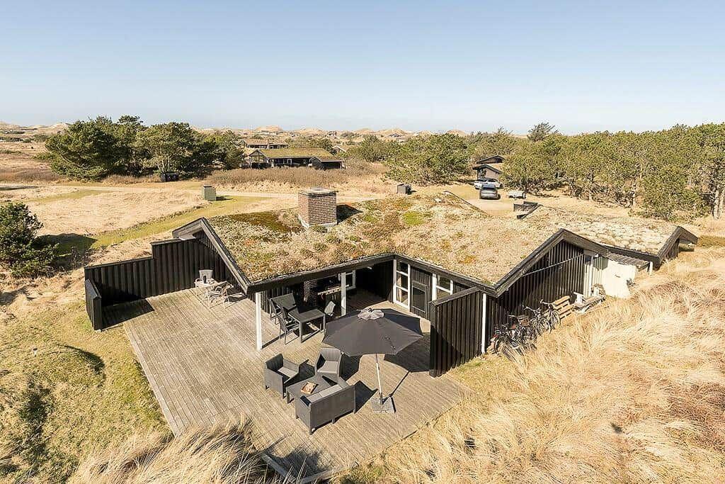 Moderne Unterkunft mit grüner Dachfläche und Holzterrasse in Dünenlandschaft.