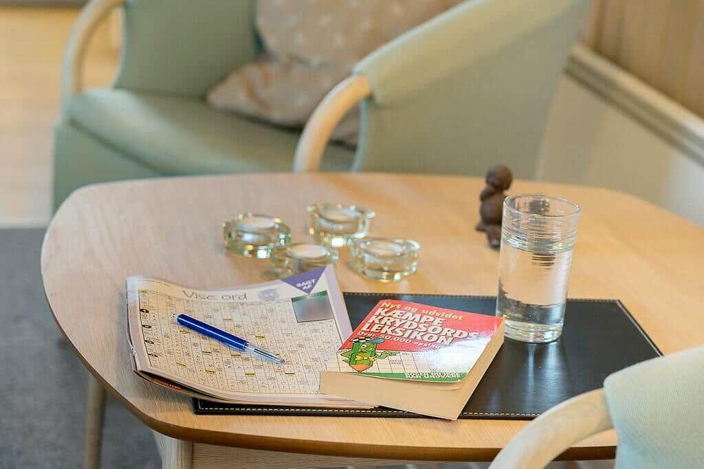 Runde Tisch mit Buch, Kreuzworträtsel und Glas Wasser.