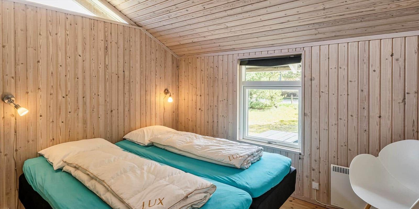 Zwei Betten mit hellblauen Matratzen und weißen Bettwäschen in einem Holzraum mit Fenster.
