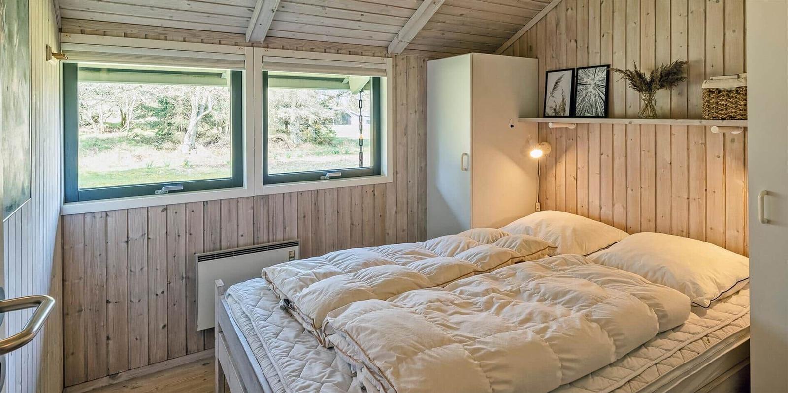 Schlafzimmer mit Bett, Fenstern und Holzwand.