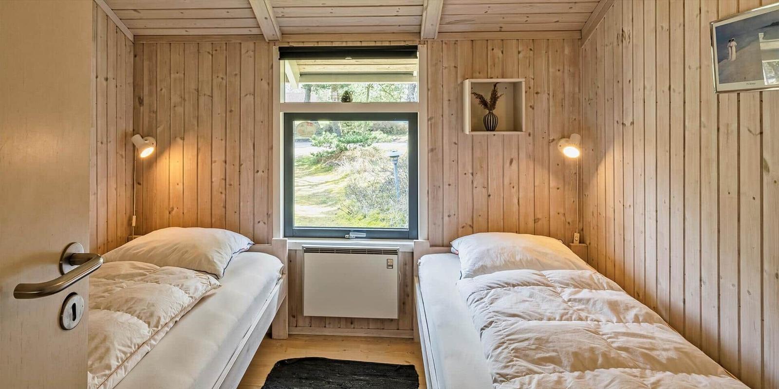 Zwei Betten, Holzwände, Fenster mit Blick nach draußen und kleine Wandregale.