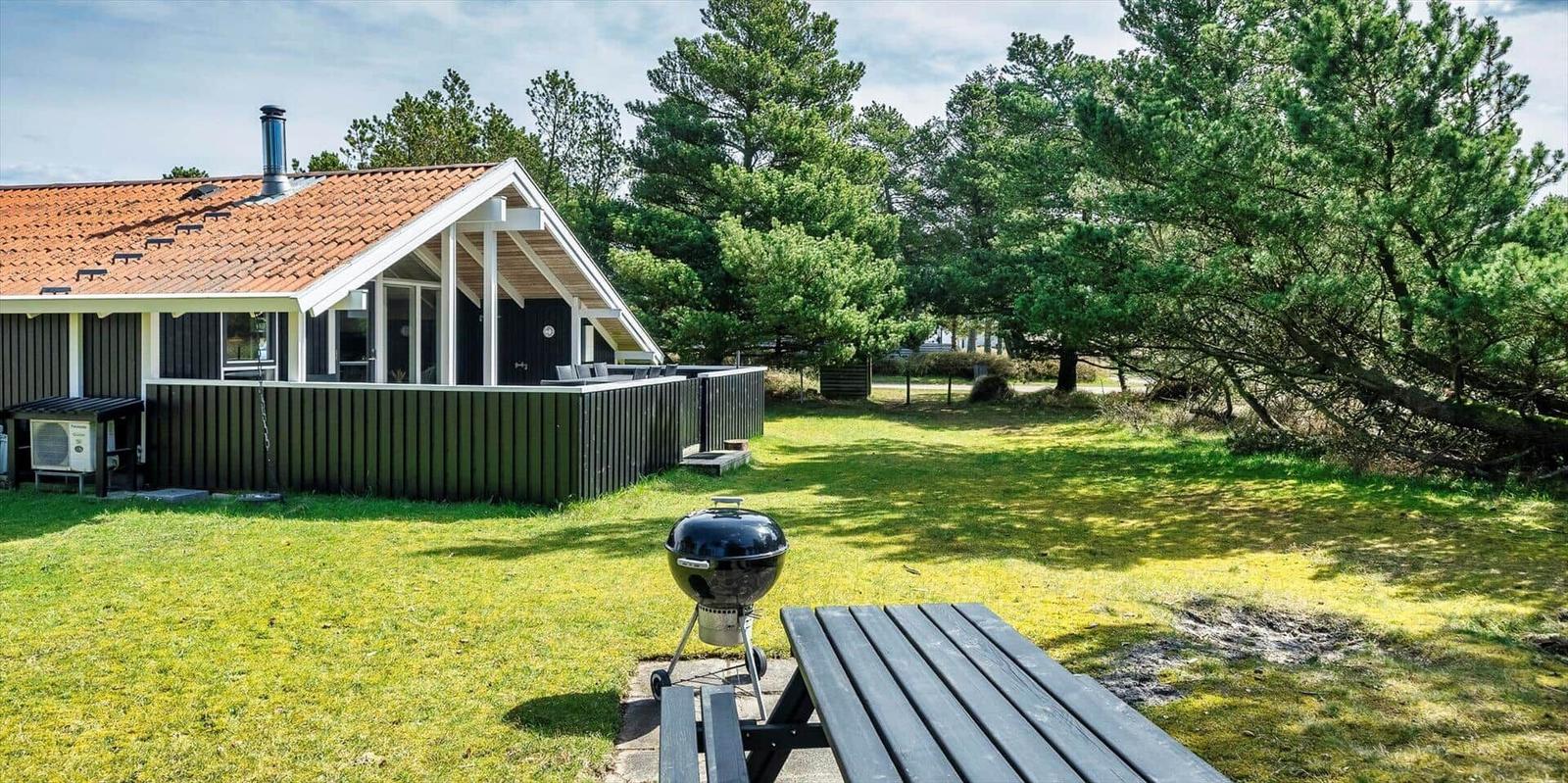Haus mit Grill und Picknicktisch auf grünem Rasen vor Bäumen.