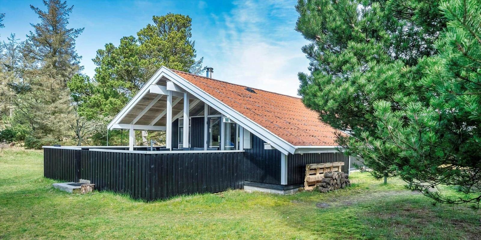 Holzhaus mit Terrasse, rotem Dach und Umgebung von Bäumen.