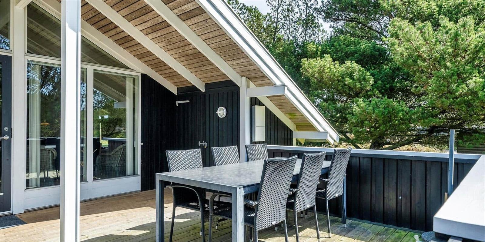 Terrasse mit Tisch und Stühlen unter Dach, umgeben von Bäumen und einer Holzwand.
