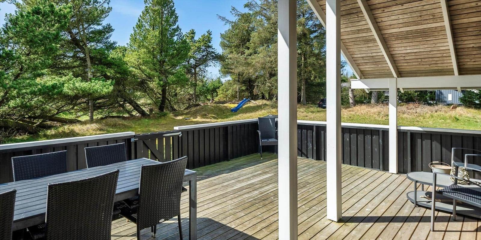 Terrasse mit Tisch und Stühlen, Blick auf Wald und Rutsche.