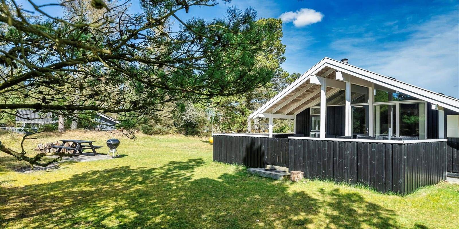 Moderne Hütte mit Terrasse, Grill und Picknicktisch im Gras.